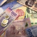 Many mixed Mexican peso bills spread over a wooden desk