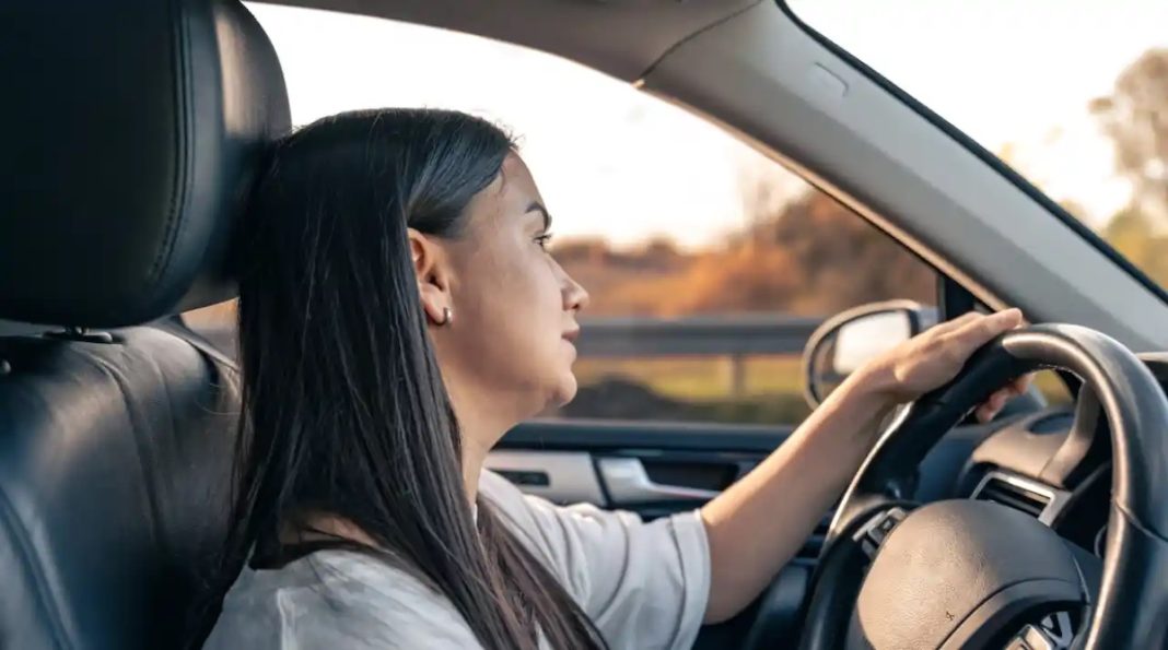 Attractive young woman driving a car, view from inside.
